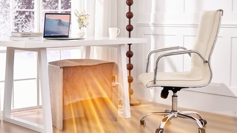 An Amazon promotional image for the Lucky Game Under Desk Heater Leg Warmer, the image depicts the heater sitting under a white office desk, with computer-generated rays of yellow light emanating from the machine
