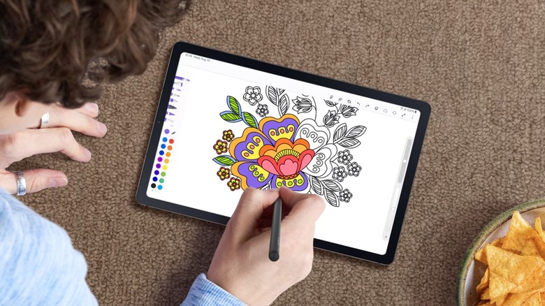 A person laying on a carpeted floor while drawing on the Galaxy S6 Lite tablet using the included S Pen