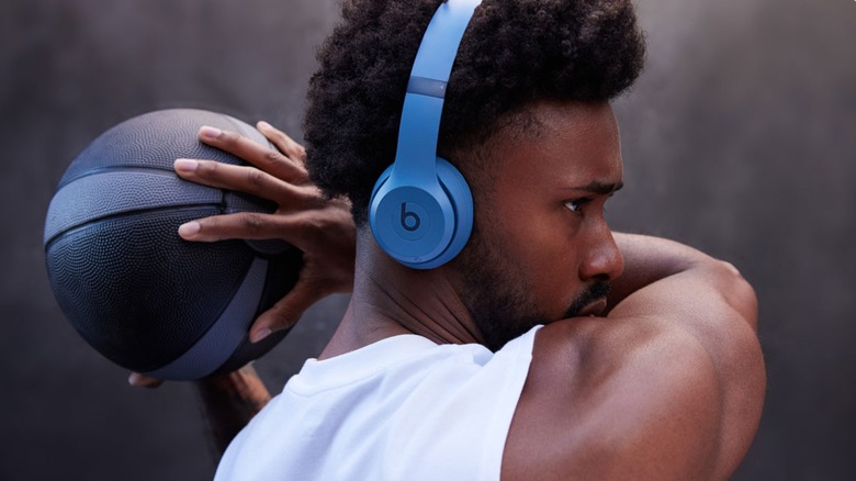 A man holding a basketball while wearing a pair of blue Beats Solo 4 wireless headphones