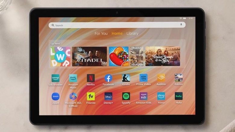 A closeup of a black Amazon Fire HD 10 tablet displaying its home screen that includes two rows of popular apps, a search bar, and a content carousel with numerous apps and media