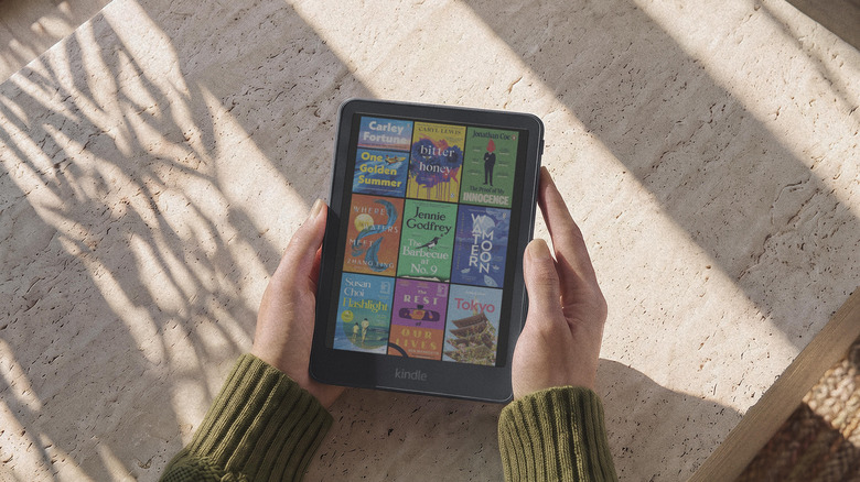 The new Kindle Colorsoft being held by two hands above a stone table