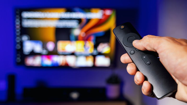 Someone using a TV remote with a smart TV on in the background.