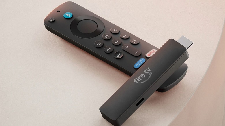A photo of the 2026 Amazon Fire TV Stick HD and its remote control, the two items are sitting a top of each other on a white table