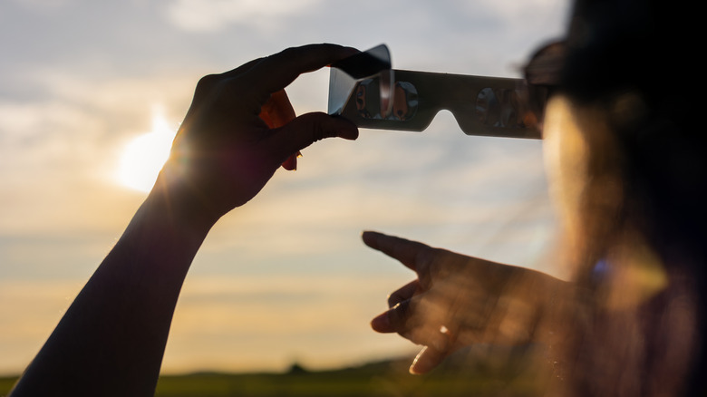 A person holding up solar eclipse glasses at a viewing event.