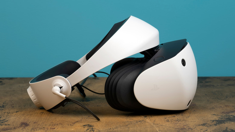 A white PlayStation 5 VR2 headset from Sony sits on a table, there is an all-blue backdrop behind the device and table