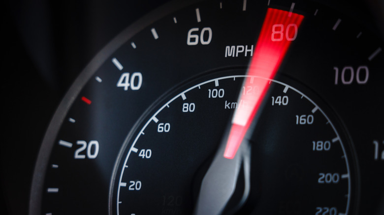 A physical speedometer showing a car's speed escalating to 80 mph