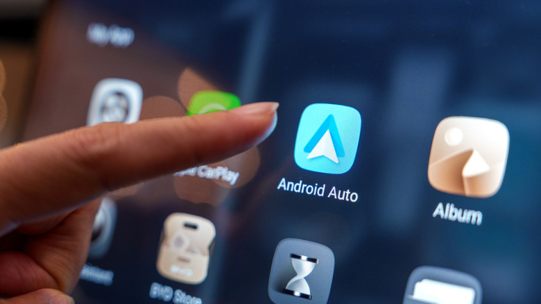 finger hovering over Android Auto app icon on car's infotainment system