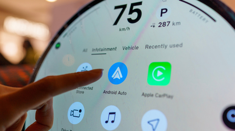 An individual using the index finger on their left hand to point to the Android Auto logo on an infotainment system