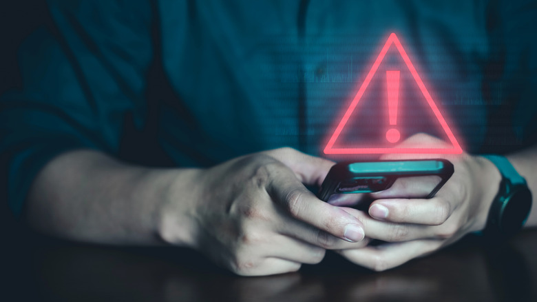 Someone using their smartphone with a warning indicator shown above it