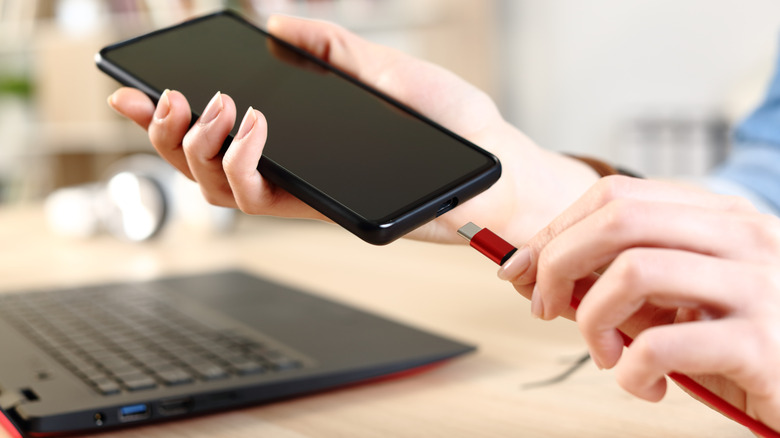 Plugging USB C into smartphone next to laptop.