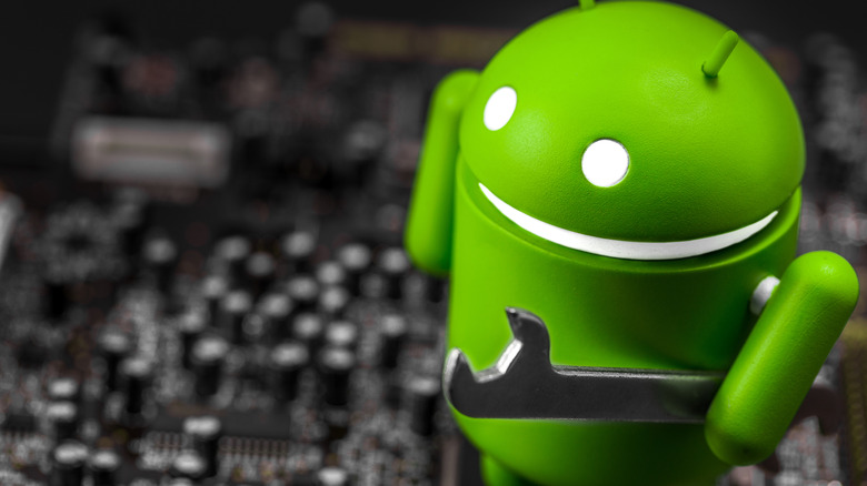Android mascot holding a wrench, standing on top of computer hardware