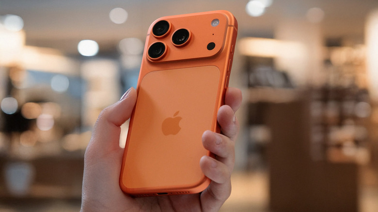 A closeup of a hand holding an orange iPhone, the background is heavily blurred