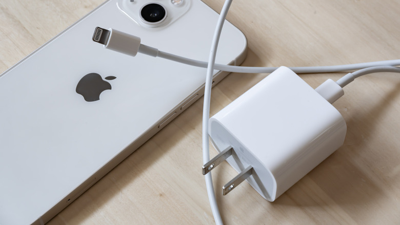 An iPhone laid next to an Apple wall charger.