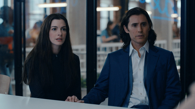 Rebekah (Anne Hathaway) and Adam Neumann (Jared Leto) sit together, looking awestruck, at a boardroom table