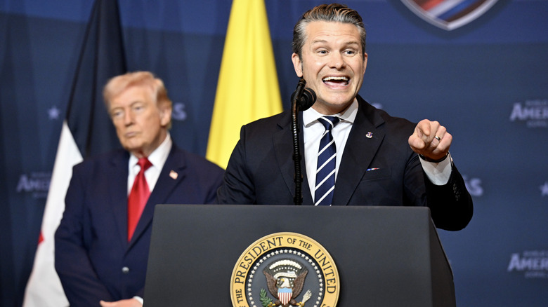 Defense Secretary Pete Hegseth points at a reporter during a speech as President Trump sits in the background