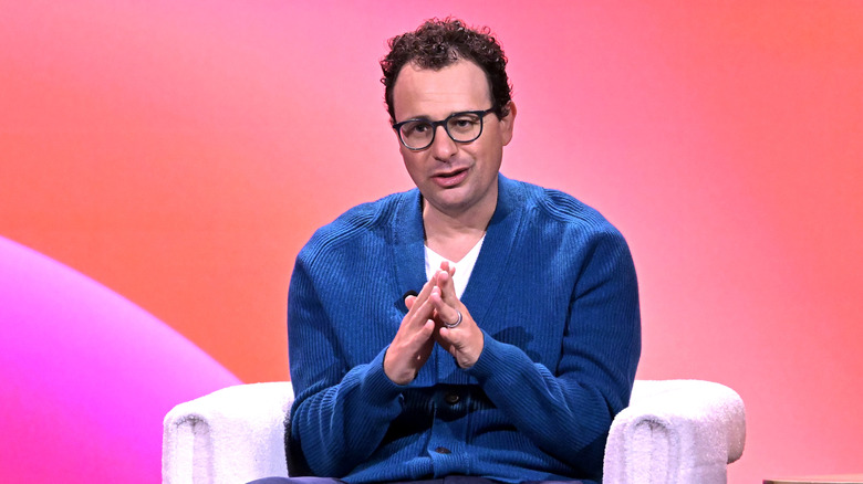 Anthropic head Dario Amodei gives a speech at a conference before a pink and orange background
