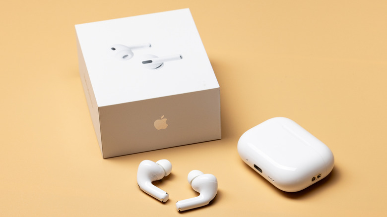 The Apple AirPods Pro 3 placed next to its packaging. All is set against a beige backdrop.