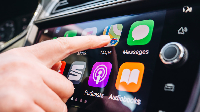 Woman pressing Apple Maps button on the Apple CarPlay main screen in modern car dashboard during driving on Spanish holiday highway