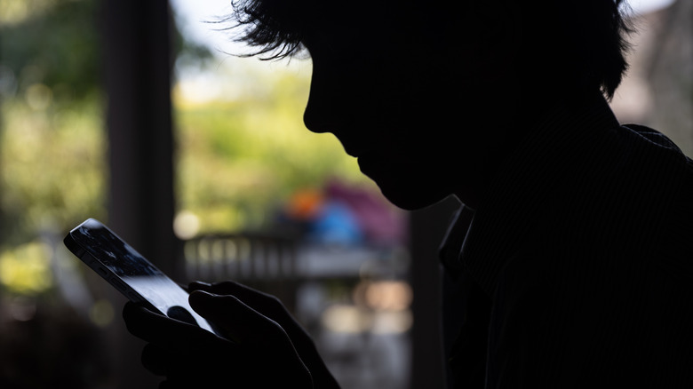A shadowy teenage boy types on his iPhone.