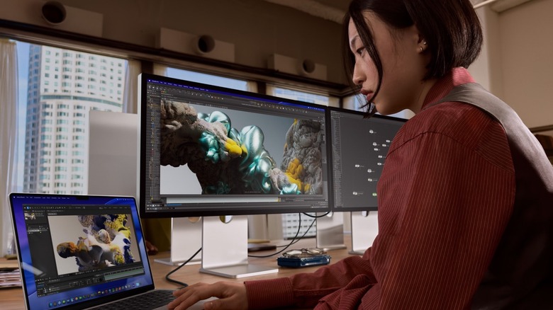 A woman editing on a MacBook Pro with two Studio Display XDR behind her