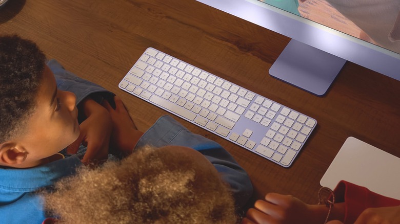 Two young individuals sit in front of a Mac, the image is heavily focusing on the Apple Magic Keyboard the two youths are using