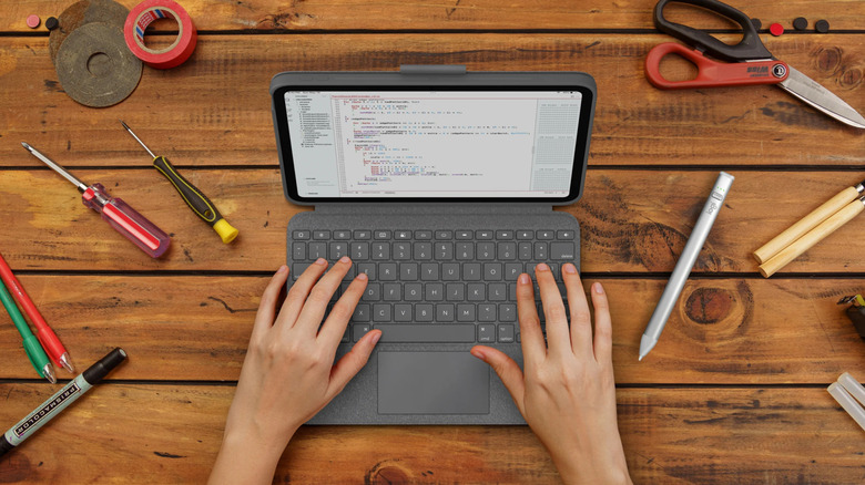 Overhead view of someone typing on a Logitech Combo Touch iPad keyboard on a wood surface with tools around it