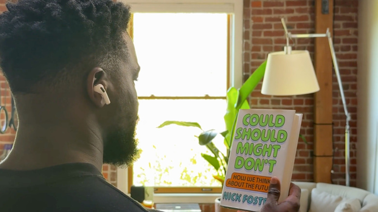 A man wearing AirPods holding up a book and looking at it