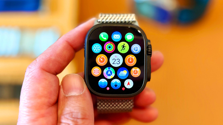 A closeup of an Apple Watch displaying its app menu as an individual holds the device in their left hand