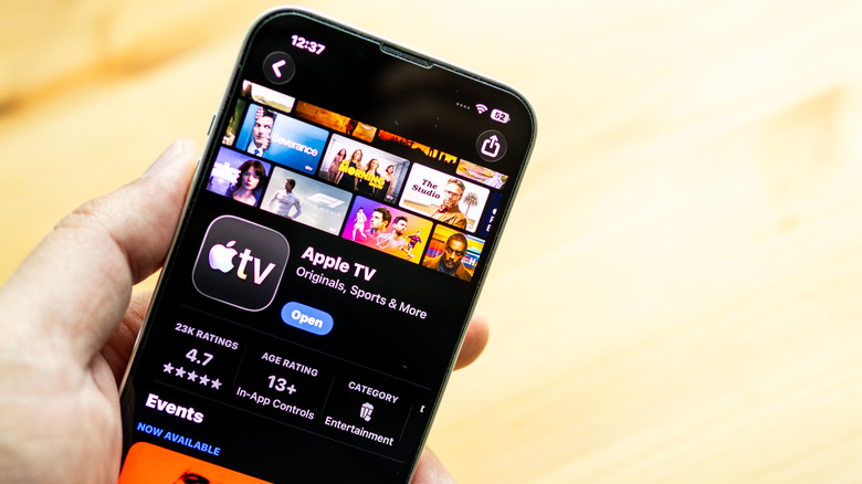 A hand holding an iPhone on a yellow background showing the Apple TV app in the App Store.