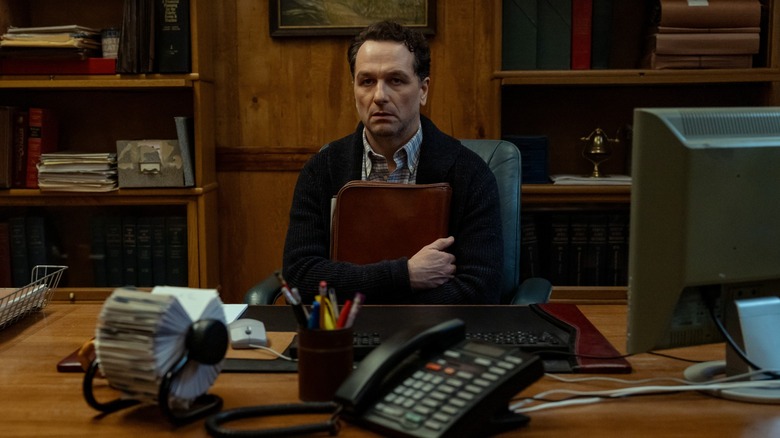 Matthew Rhys sitting at a desk while clutching what appears to be a brown leather briefcase in a scene from the Apple TV series "Window's Bay"