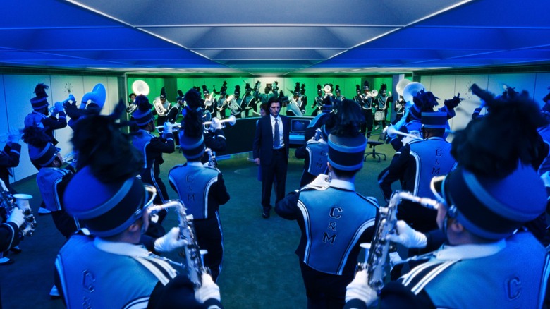 An image from the series "Severance" in which character Mark S. (Adam Scott) stands in the middle of an office as he is surrounded by an entire marching band.