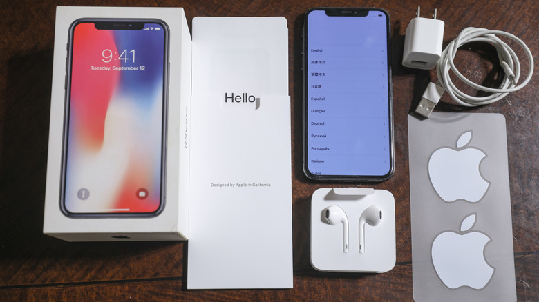 The iPhone X retail box and its contents, including the iPhone X, accessories, and Apple stickers.