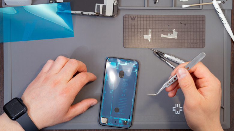 A person holding a repair tool to fix an open iPhone body