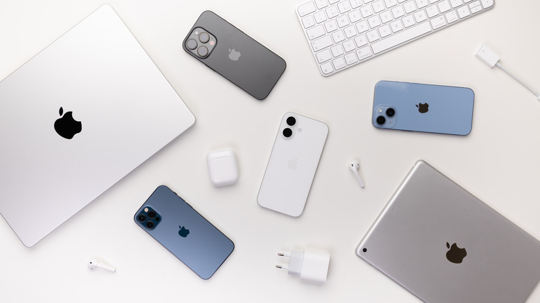 Apple devices like macbook, iphones, iPad, keyboard, airpods, charging adapter, and cable laid out on a white table