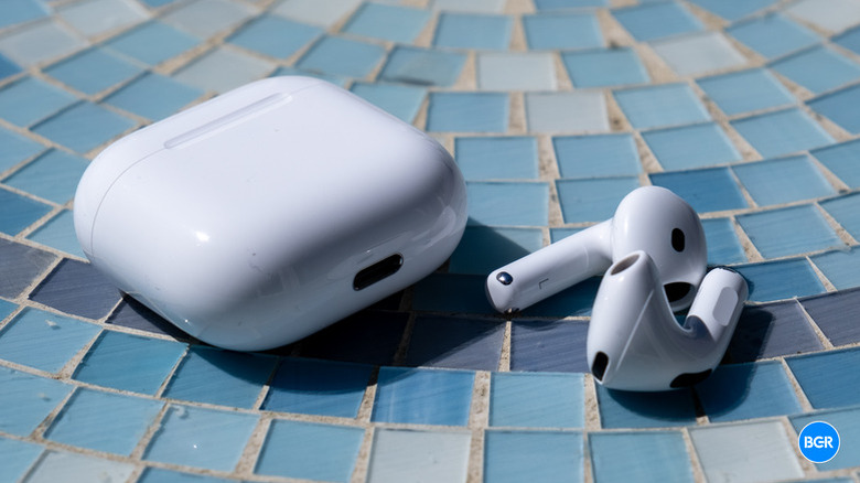 A pair of AirPods 4 sitting next to their charging case on top of a blue, box-patterned table