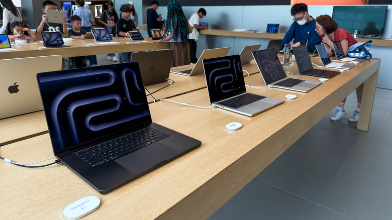 Apple Store employees assist customers browsing MacBook laptop