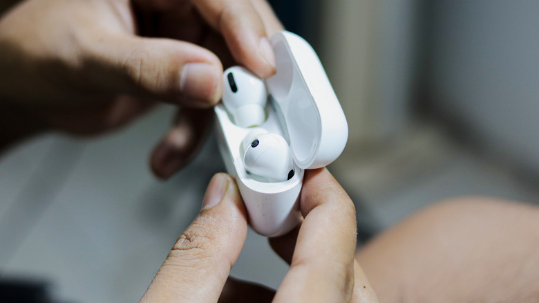 A close-up of a person's hands holding open a white AirPods Pro case, revealing the wireless earbuds inside