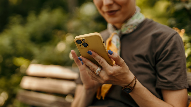 woman wearing a t-shirt and neck scarf uses an iPhone in the park