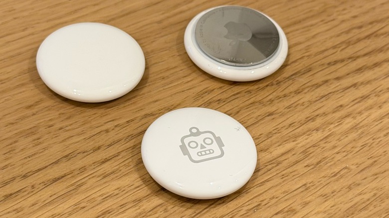 Several AirTags on a desk. One of them has a robot engraved.