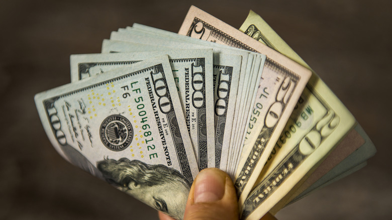 a hand holding several US dollar bills