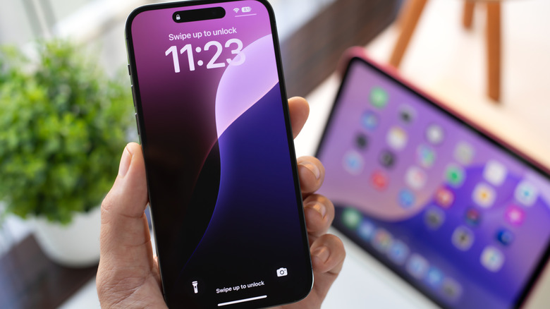 An iPhone in hand with an iPad in the background.