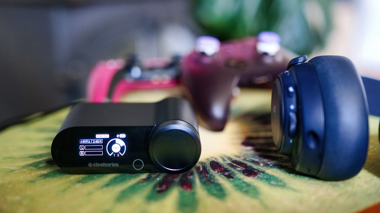 The Arctis Pro Omni Playhub device showing the mixer screen in use, on a kiwi cushion next to the headset
