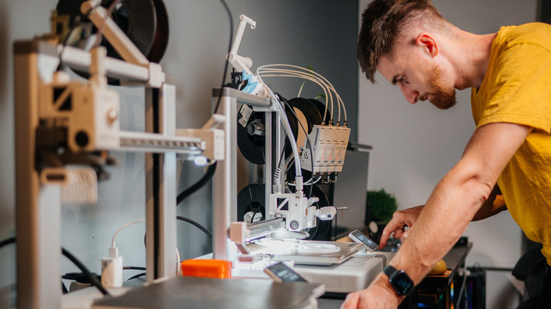 Person adjusting a 3D printer while a print is in progress