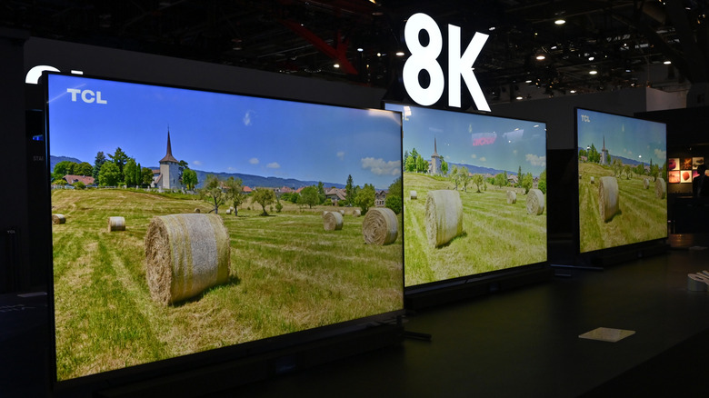 TCL 8K displays in a line at a show with an 8K sign above them. The TVs are showing hay bales in a field.
