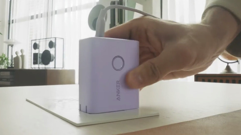a hand grabbing a small Anker charging station on a table