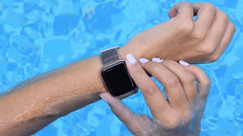 A closeup of someone's hands engaging the Apple Watch's Digital Crown while in a pool