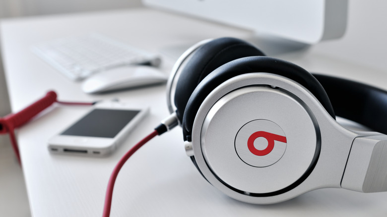 A pair of original Beats headphones sitting on a desk with a phone and computer in the background