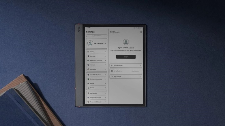A Boox e-reader and e-ink tablet next to some paper journals on a blue surface.