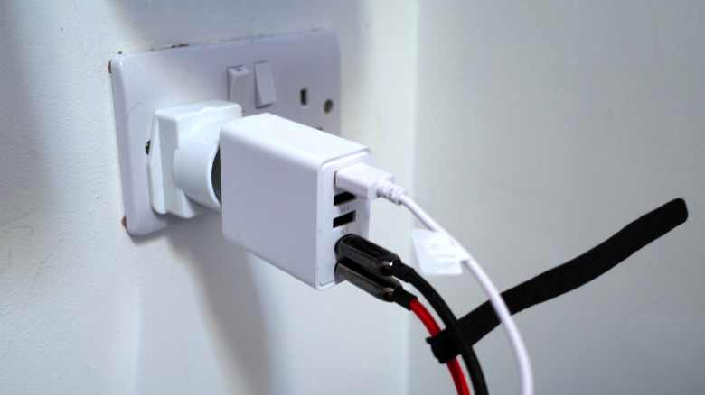 A multiport wall adapter plugged into a British wall outlet, with one of three USB Type-A and both USB-C ports in use.
