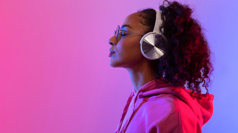 a woman listening to headphones on a pink and purple background.